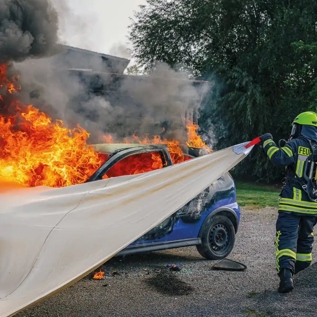 Tűzoltó oltja a lángoló kék autót tűzoltó takaróval.